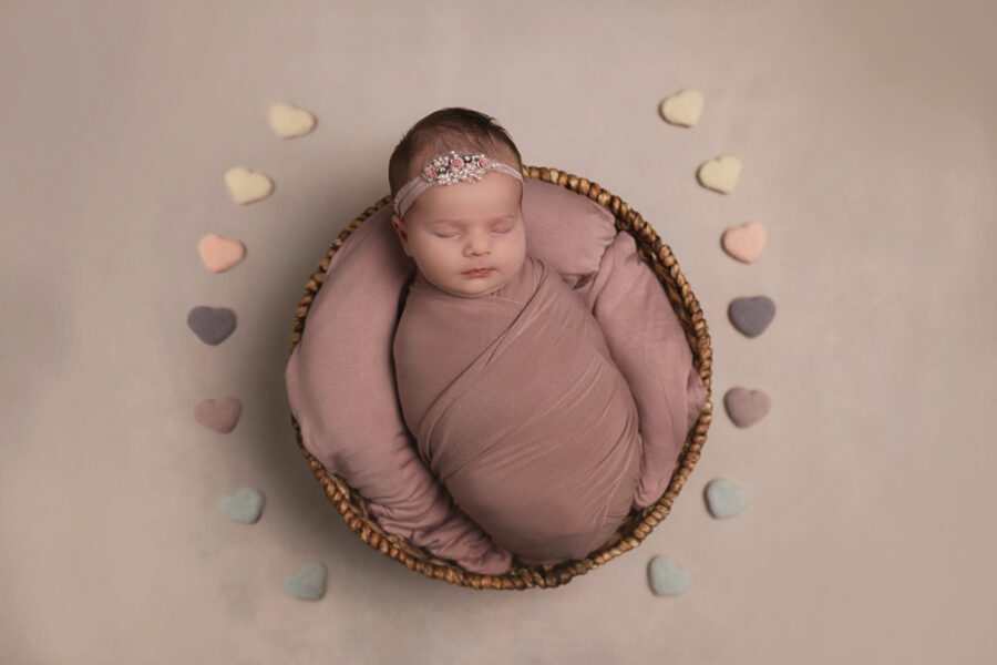 Dallas Newborn Photographer photographing baby girl wrapped in pink with heart decorations.